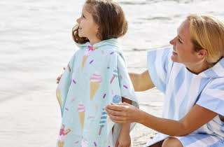 En kvinne og en liten jente som står på en strand, begge har på seg strandponchoer