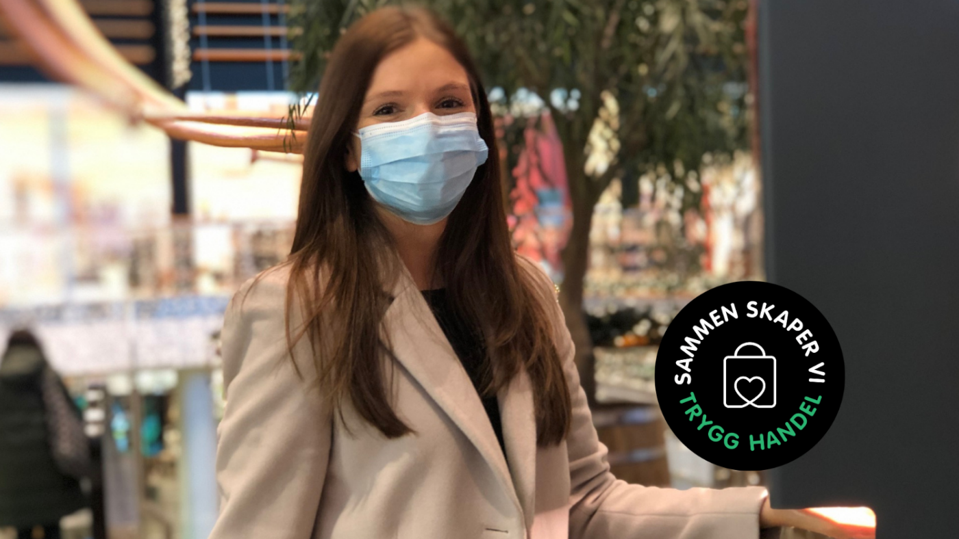Trygg Handel. Jente med munnbind som spriter hendene ved antibac-stasjon.