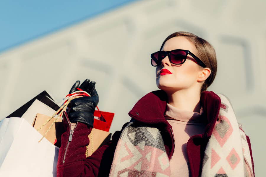 Dame med shoppingposer og solbriller ser mot himmelen