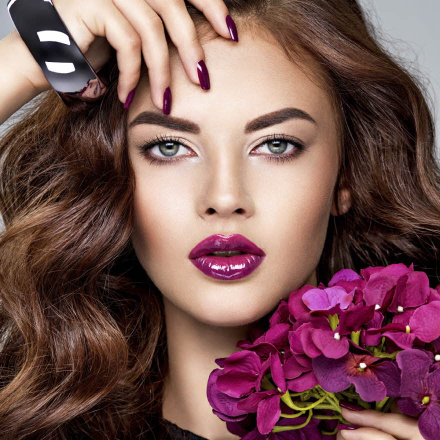 Dame med lilla lepper og holder en lilla blomst til ansiktet