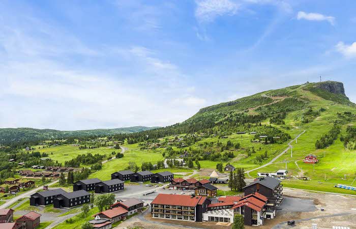 Oversiktsbilde over Høyfjellstunet på Skeikampen man ser bygninger i forgrunnen og det flotte fjellet Skeikampen i bakgrunnen.