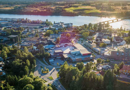 Luftfoto med AMFI Årnes i forgrunn og omgivelser med elv og landskap i bakgrunn, i mykt kveldslys.