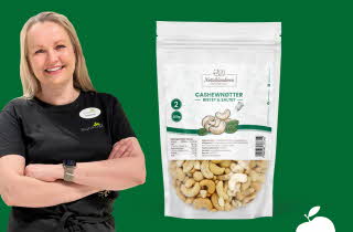 Kvinne som står med armene i kors ved siden av en pose med cashewnøtter.