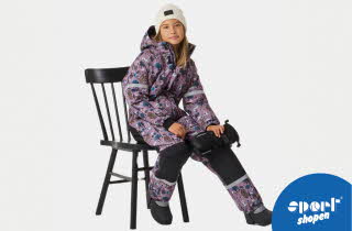 Jente sitter på en stol iført mønstret lilla vinterdress med refleksdetaljer og vinterstøvler.