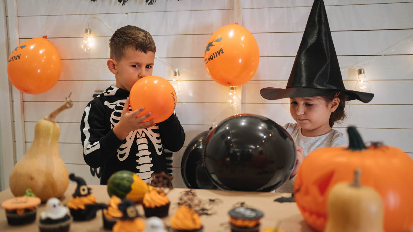 To barn blåser opp sorte og oransje ballonger til halloweenfest