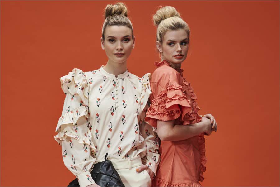 Oransje bakgrunn med to damer, en med hvit mønstret topp og en med oransje kjole