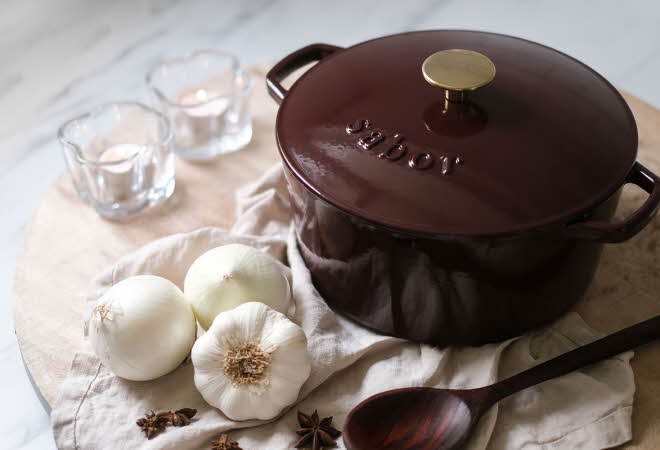 En støpejernsgryte fra Sabor som står på en kjøkkenbenk med hvitløk ved siden av.