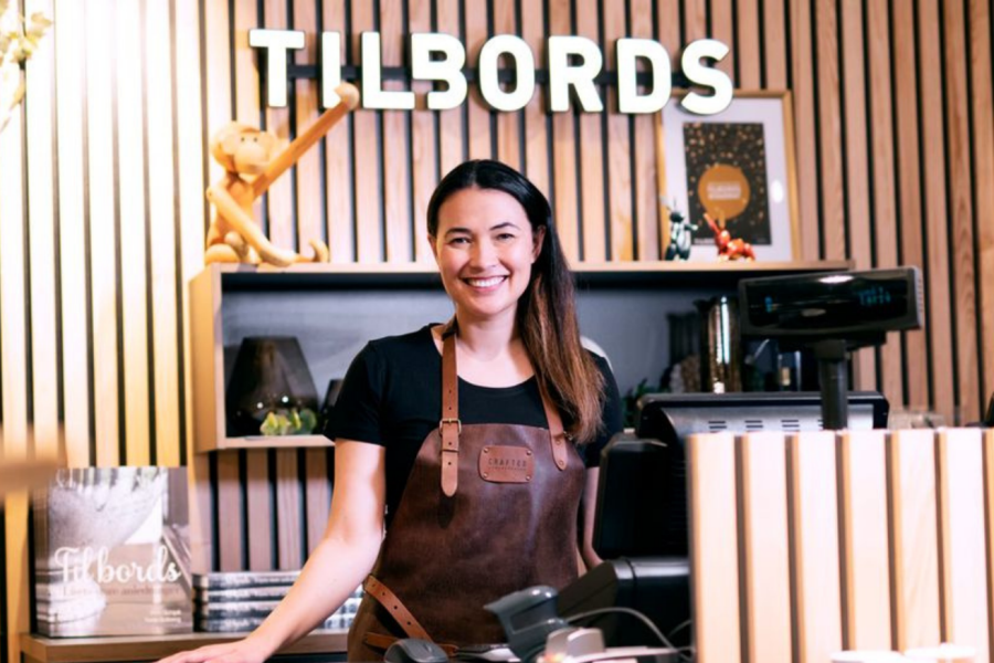 Selger fra TilBords som står bak kassen smilende