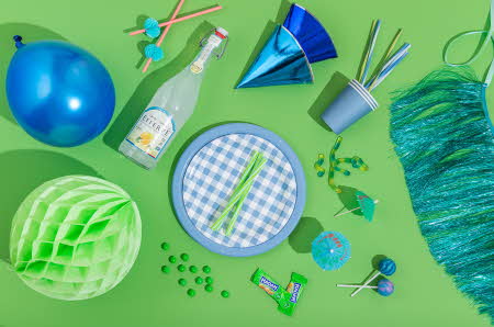 Diverse festgjenstander, som ballong, party hatter, små paraplyer med mer, som ligger på en grønn bakgrunn