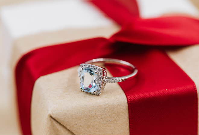En Jacqueline diamantring som ligger oppe på en innpakket gave.