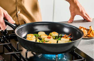 Nærbilde av en person som steker kamskjell i en stekepanne.