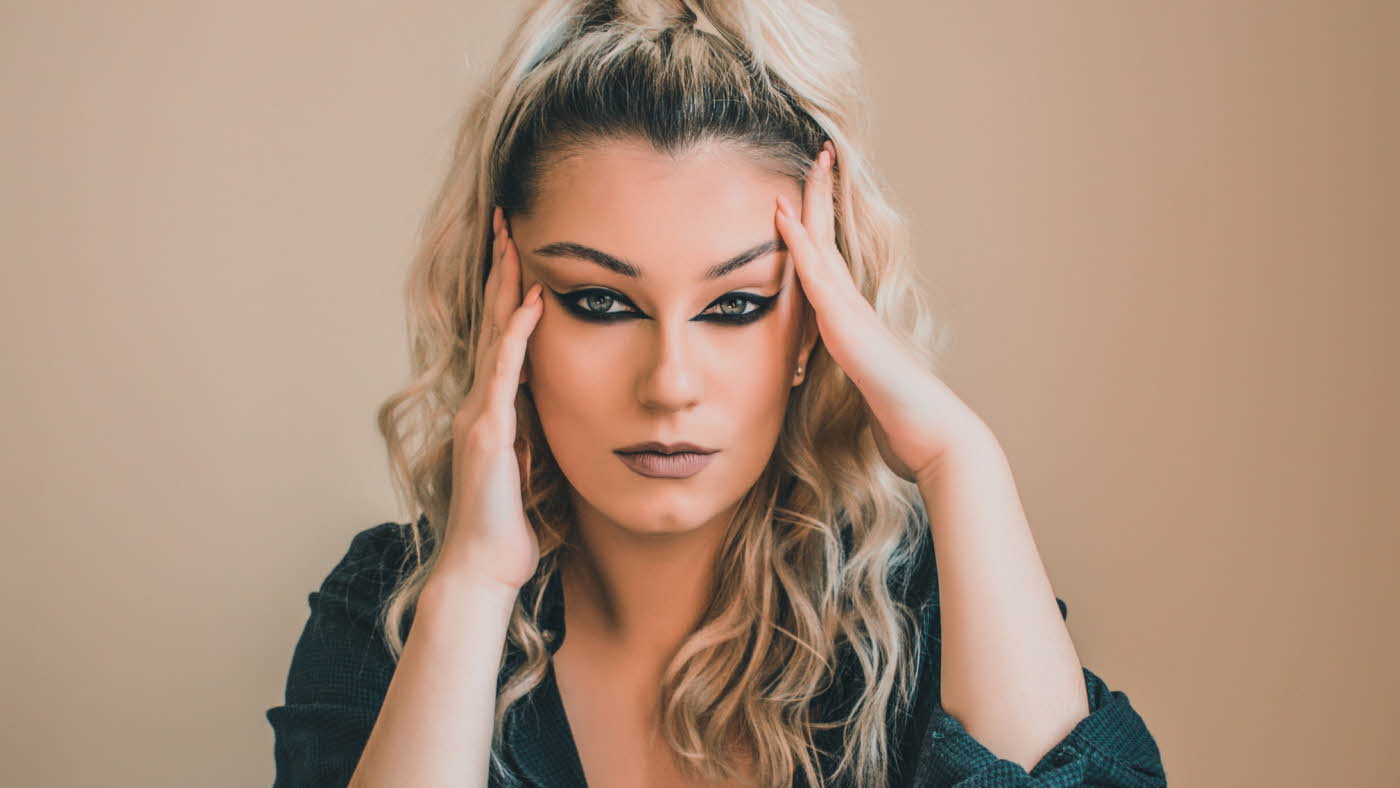 Kvinne med oppsatt hår og reversed cat eye-sminke som ser i kamera