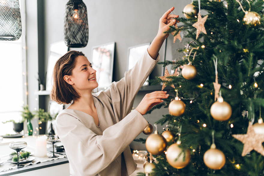 Nærbilde av dame som smiler mens hun pynter juletre med julekuler av gull