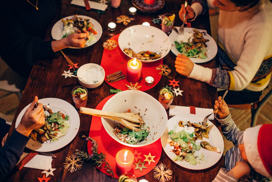 Folk som spiser vegetar julemiddag rundt et bord med rød duk