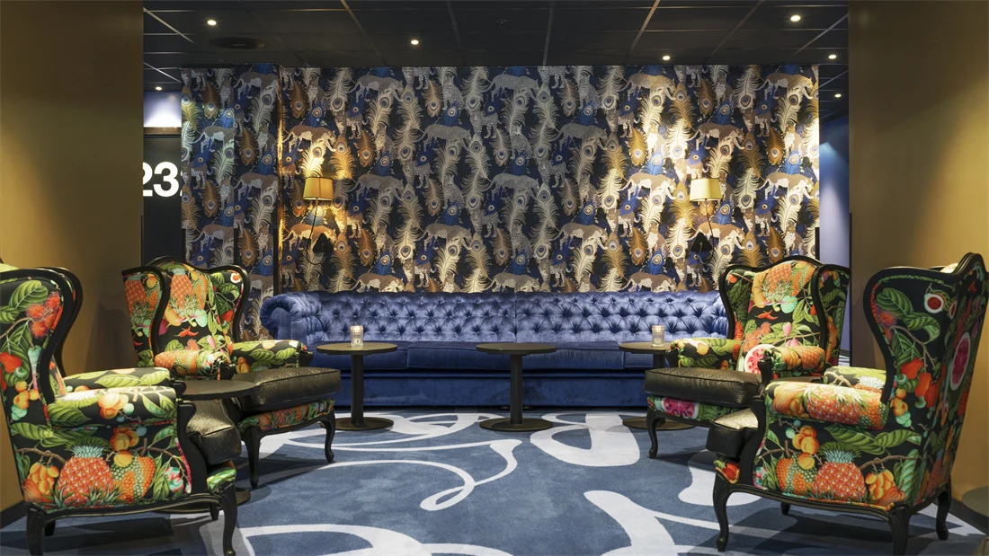 Teppe med mønster og påfugl-tapet, mønstrede lenestoler og blå sofa i lounge på Thon Hotel Terminus i Oslo sentrum nær Jernbanetorget