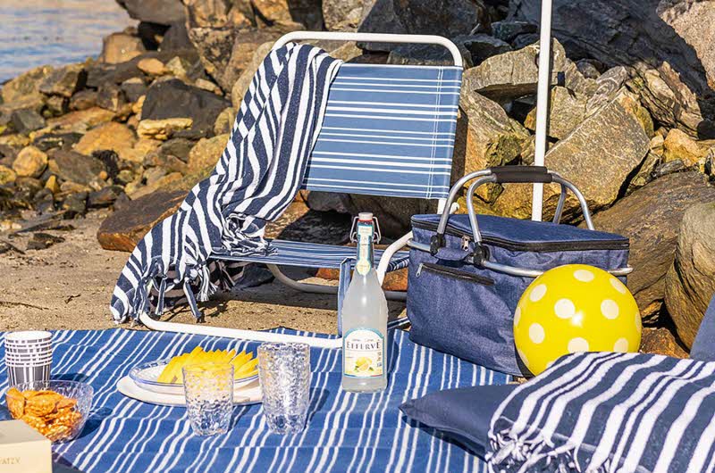sitteplass på stranden med lenestol, kjølebag, sitteunderlag og teppe i stripete mønster