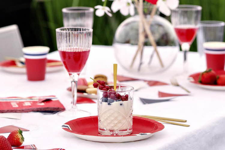 Dekket 17. mai-bord med tallerkener, servietter, glass og bestikk. Glass med krem og bær