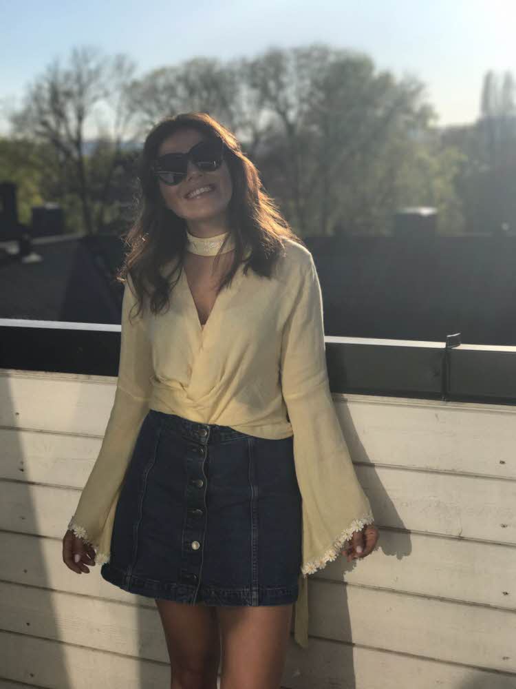 Brunette smiler til kamera iført gul topp og kort dongeriskjørt