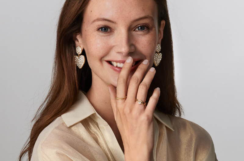 Dame poserer med hjerteformede diamant øredobber og to gullringer