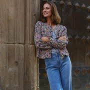 En kvinne lener seg på en gammel bygning, hun har på seg en blomstrete jakke og jeans