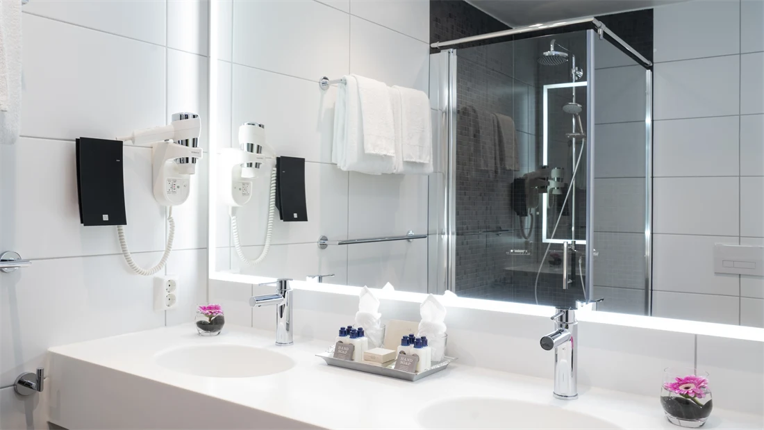 Dobbel servant og stort speil som reflekterer dusj på bad i suite på Thon Hotel Storo i Oslo