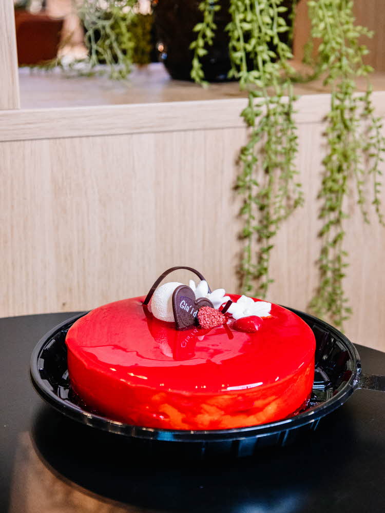 Kaffelatte og et kakestykke med sjokolade hvor det står "Gla' i deg" Rød kake med pynt