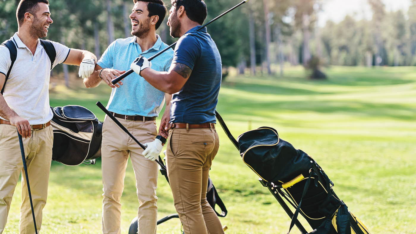 Smilende menn med golfutstyr og klær på golfbane