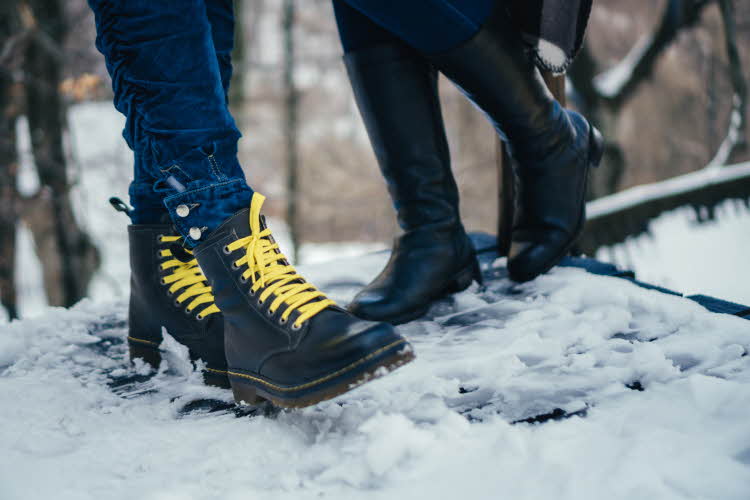 To personer med svarte boots med snøring og støvletter står i snøen. 
