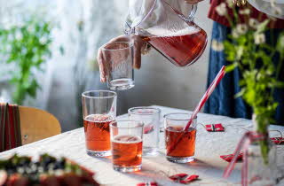 Person som heller rød drikke fra en glassmugge i et glass på et pyntet bord.
