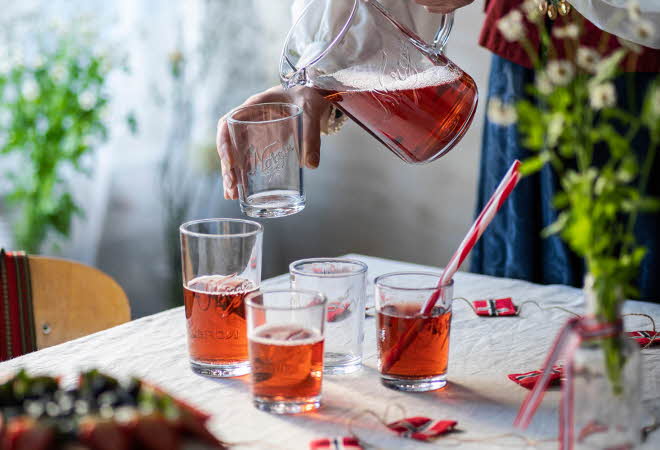 Person som heller rød drikke fra en glassmugge i et glass på et pyntet bord.