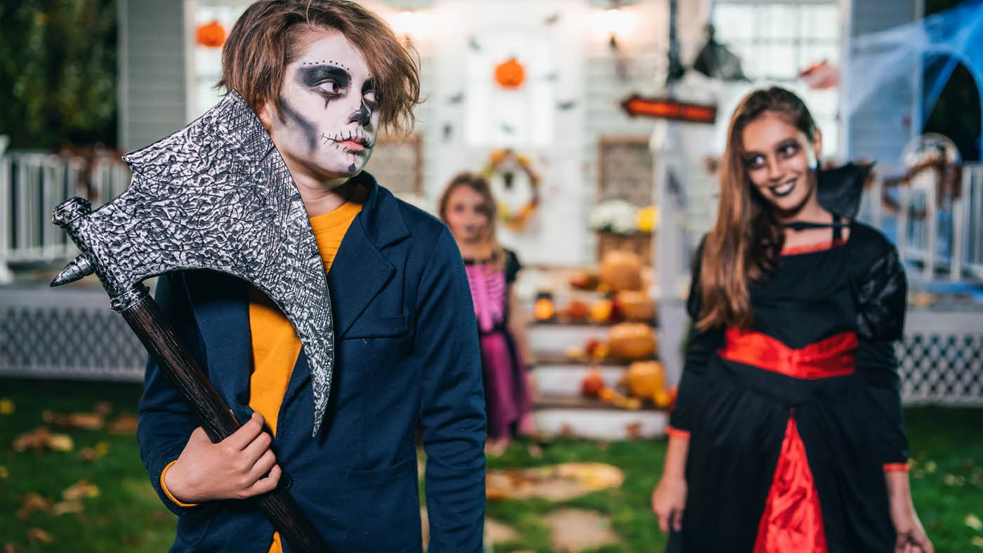 Tre barn som er sminket og utkledd til halloween og står i en hage med gresskar i bakgrunnen