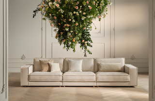 Beige sofa med fire seter og en hengende blomsteroppsats over.