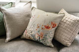 Tre dekorative puter på en sofa, en med blomsterdesign, en grønn og en beige.