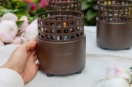 En hånd holder på en lykt fra Tenderflame som står på en bord