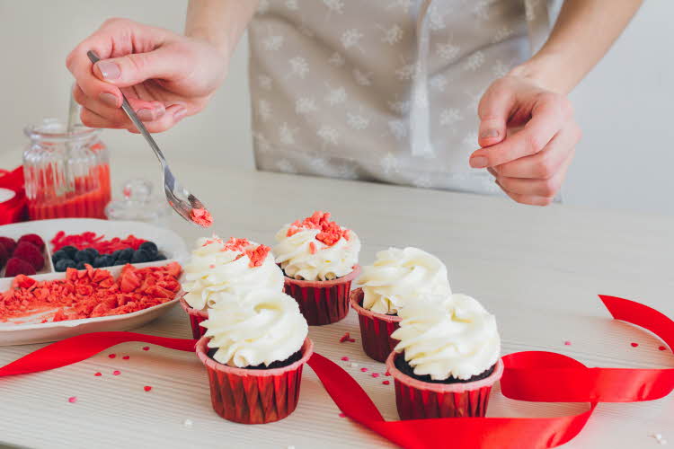 Person legger rosa strøssel lys glasur på sjokolademuffins