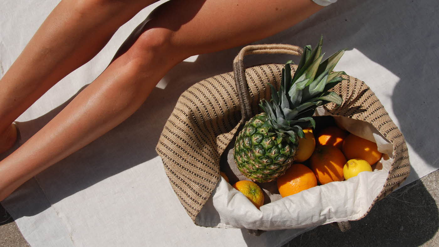 Nærbilde av solbrune legger og strandveske med frukt