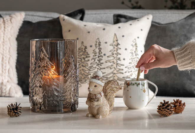 En hånd som rører i en kopp som står på et bord pyntet til vinter.