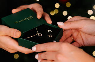 Nærbilde av et par hender som gir et annet par hender en boks med et smykkesett.