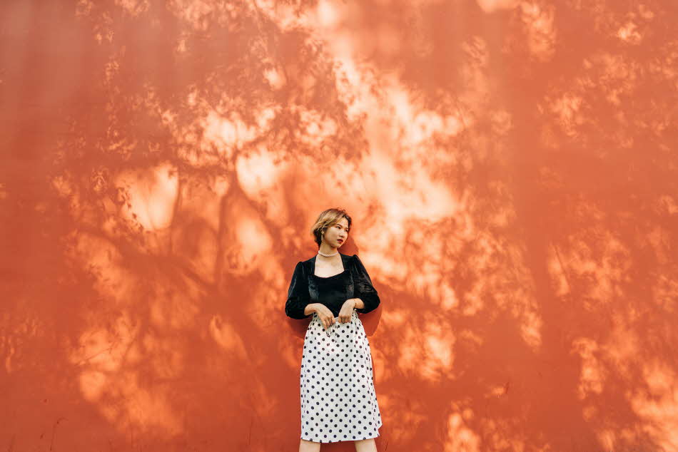 Dame med sort fløyelstopp og hvitt polkadotskjørt står inntil oransje vegg