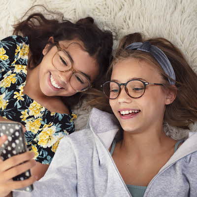 to unge jenter med briller som ligger på gulvet med mobil i hånden