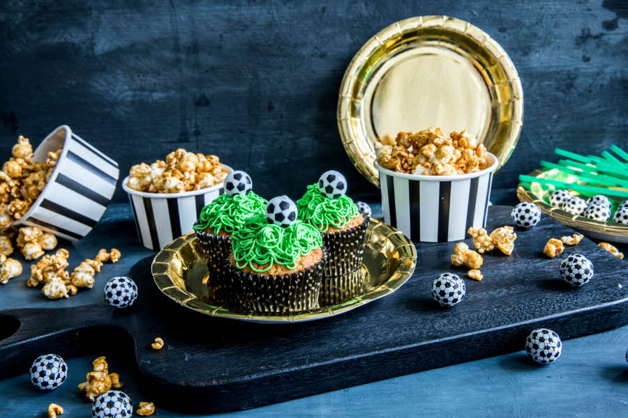 Bord med fotballcupcakes på gulltallerkener og popcorn i skåler 