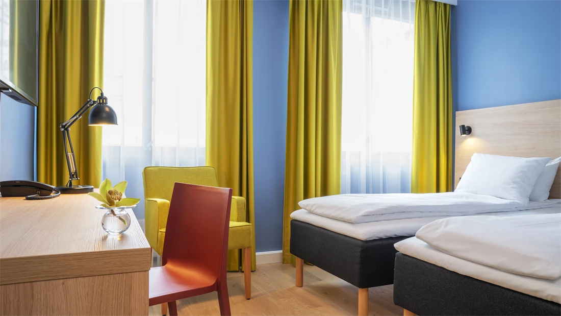 Separate senger, blå vegger, gule gardiner og skrivebord på standard rom twin på Thon Hotel Astoria