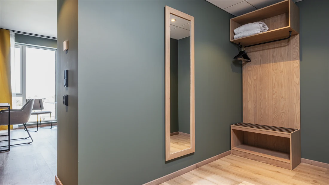 Inngangsparti i superior rom med garderobe, helspeil, grønne vegger og parkett.