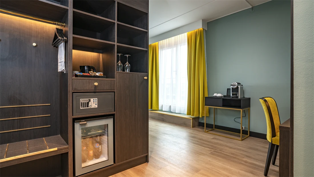 Skap, skrivebord, gul lenestol, vindu, grønne/turkise vegger, kaffemaskin, minibar