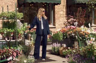 En kvinne i denim bukser og denim jakke står omringet av blomster i en blomsterbutikk