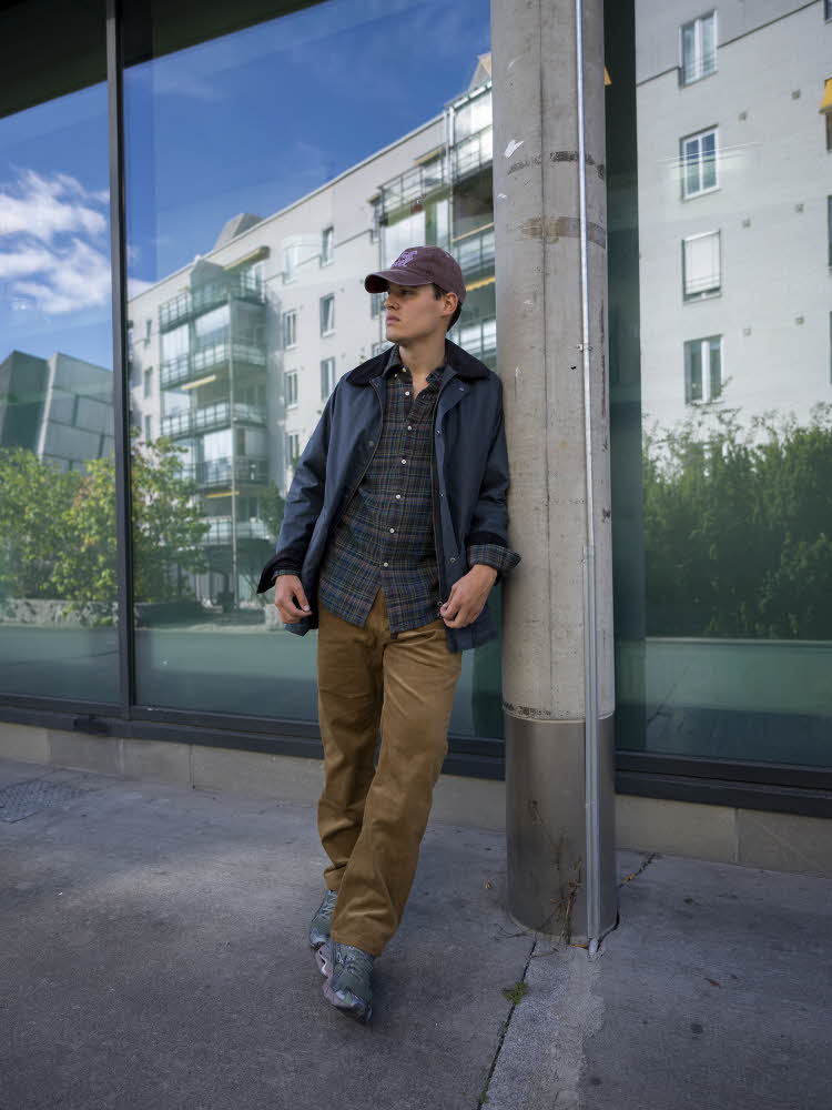 Mann i blå caps, blå ytterjakke, rutete skjorte, brune bukser og sneakers.