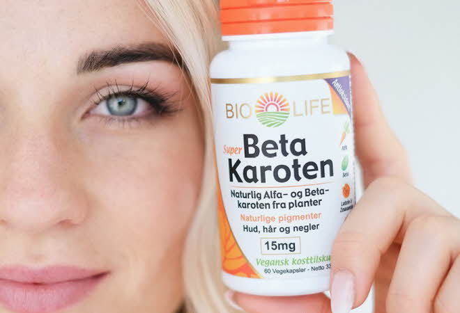 En kvinne holder en boks med betakaroten opp ved siden av ansiktet