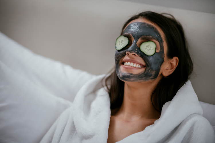 Kvinne i morgenkåpe med ansiktsmaske og agurk på øynene