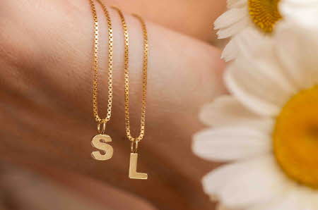 En hånd som holder to smykker i gull med bokstaven S og L
