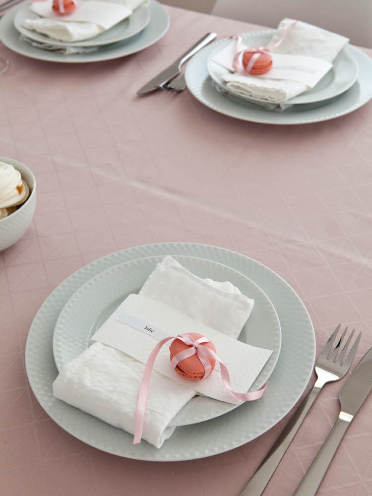 Steg fem - Bord dekket med tallerkener og hvit linservietter og en rosa makron og bestikk på en rosa duk  Steg 6 -  Bord dekket med tallerkener, hvit linservietter, farerike blomster på rosa makron på en rosa duk